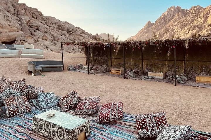 Un camp dans le désert de style bédouin situé au milieu des falaises de montagne avec des sièges ombragés, des coussins colorés et des tapis tissés à Charm el-Cheikh
