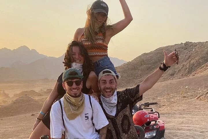 Trois touristes souriants posant à côté d'un quad sur fond de désert montagneux à Charm el-Cheikh