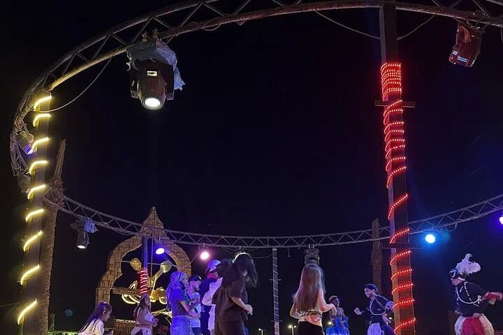 Un spectacle nocturne dans le désert sur une scène bien éclairée avec des artistes et des invités rassemblés sous des lumières décoratives à Charm el-Cheikh