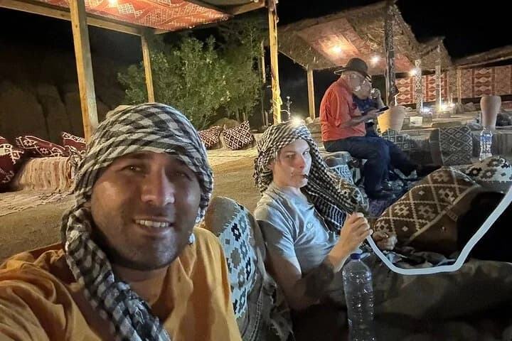 Les invités de la visite se détendent sur des coussins à motifs lors du camp nocturne dans le désert de Charm el-Cheikh, portant des foulards traditionnels