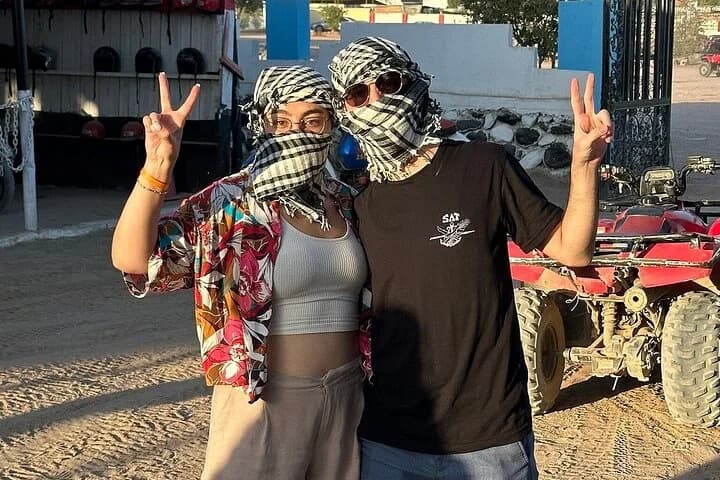 Deux invités au safari posant à côté de quads VTT garés avec des signes de paix à la base touristique de Charm el-Cheikh, vêtus de foulards de style désertique