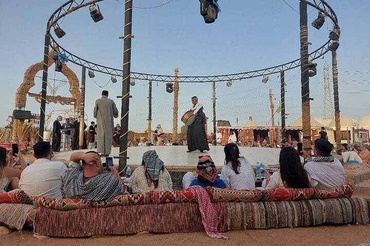 Des invités assistent à un spectacle culturel bédouin en direct sur une scène extérieure, assis sur des bancs rembourrés traditionnels dans le désert de Charm el-Cheikh