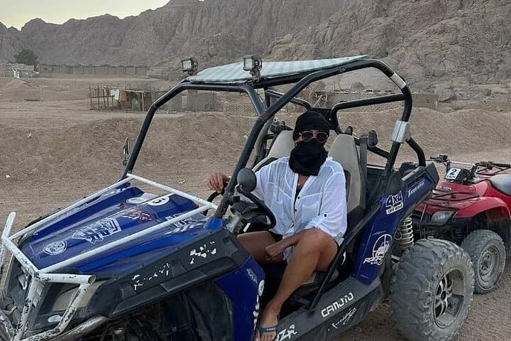 Une femme masquée assise dans un buggy tout-terrain bleu entourée de montagnes rocheuses et d'autres véhicules de safari à Charm el-Cheikh