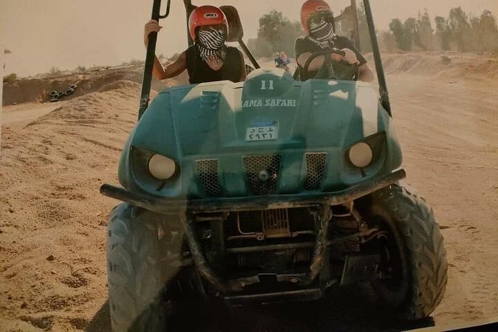 Deux passagers casqués chevauchant ensemble dans un buggy tout-terrain turquoise à travers le terrain désertique sablonneux de Charm el-Cheikh