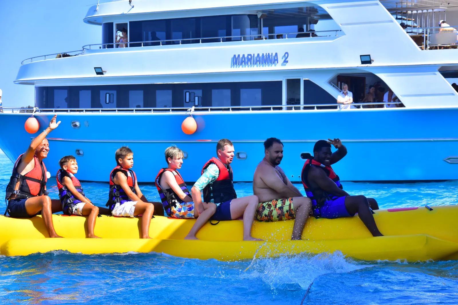 Family laughing on a banana boat ride beside a yacht on a Hurghada boat trip in the Red Sea
